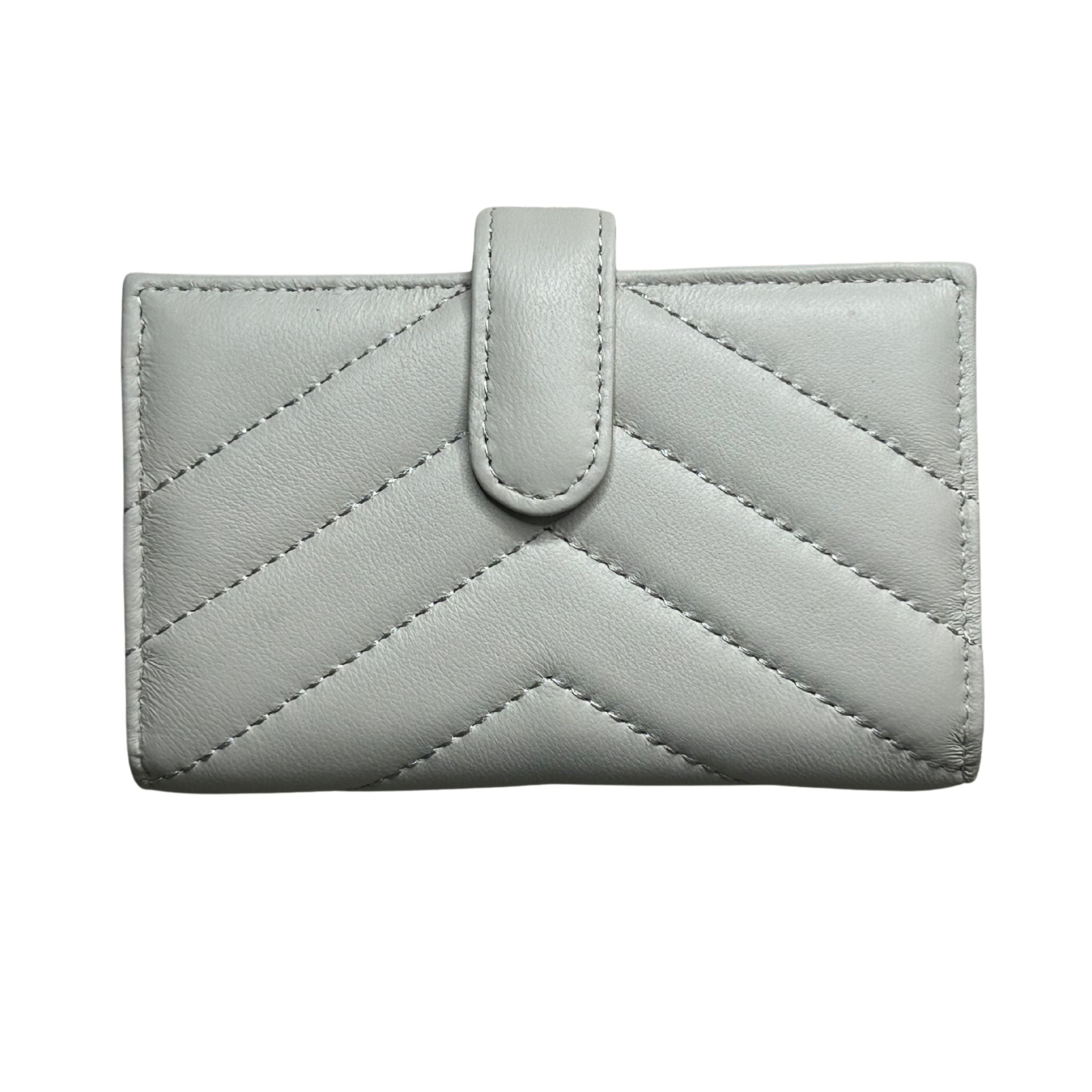 A white/ivory quilted lambskin leather wallet with a chevron pattern and a central tab closure