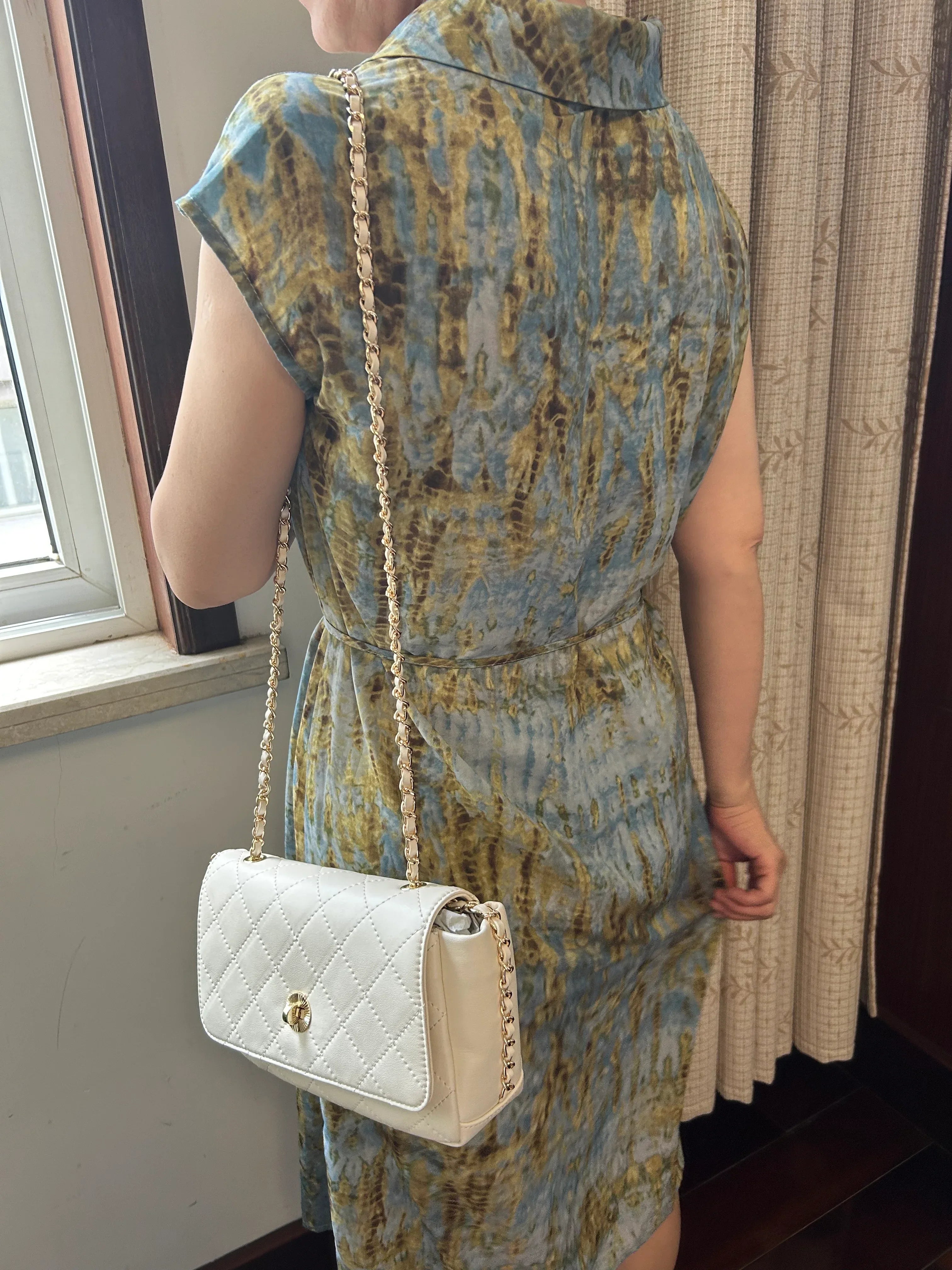 Woman wearing ivory quilted leather crossbody bag with chain strap